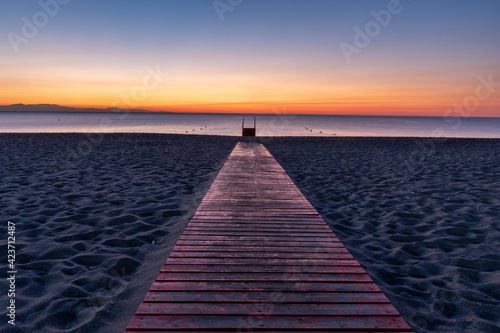 Fototapeta Naklejka Na Ścianę i Meble -  A wooden, red footbridge leading to the sea