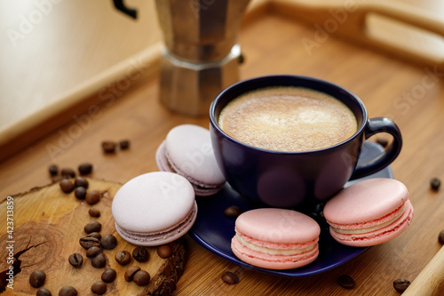 Cup of coffee, macaroons, and coffee beans on a platter and geyser coffee maker on a wooden tray