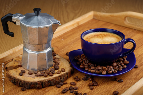 Cup of coffee and coffee beans on a platter and geyser coffee maker on a wooden tray