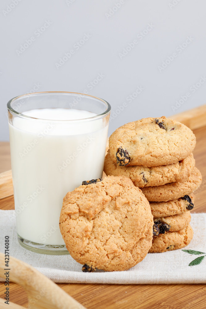 A glass of milk and cookies with raisins on a wooden tray A glass of milk and cookies with raisins on a wooden tray