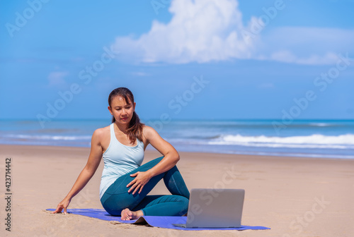 people, fitness, sport and healthy lifestyle concept - asian woman making yoga pose on tropical beach with laptop