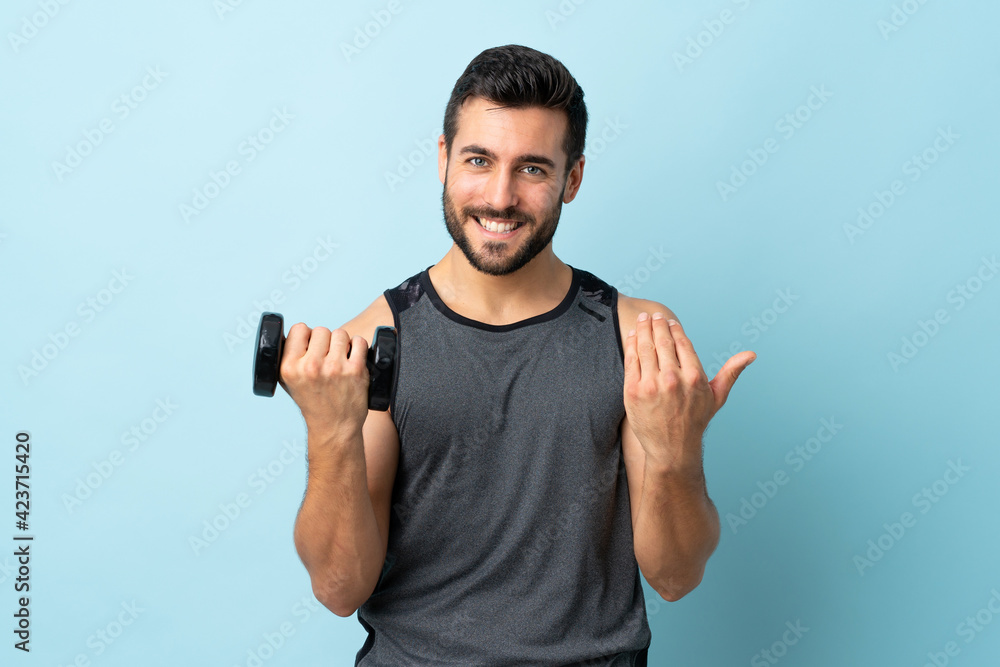 Young sport man with beard making weightlifting inviting to come with hand. Happy that you came Young sport man with beard making weightlifting inviting to come with hand. Happy that you came