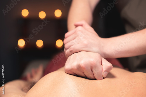 male masseur with his hands kneading muscles on his back, close-up
