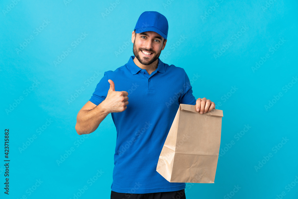 Delivery man with beard isolated on blue background with thumbs up because something good has happened Delivery man with beard isolated on blue background with thumbs up because something good has happened