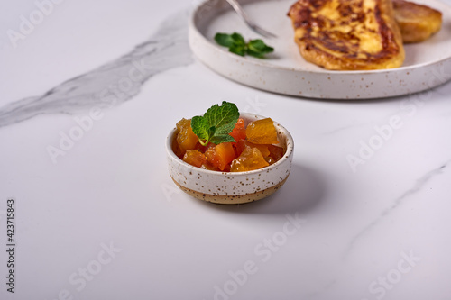 Melon jam with mint in a small bowl on a light background. In the back is Torrihas. Copy space