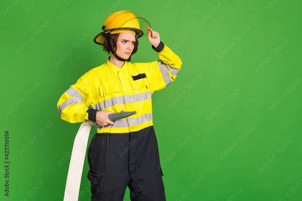 Photo of pretty confident fire lady workwear arm yellow helmet holding water hole looking empty space isolated green color background Photo of pretty confident fire lady workwear arm yellow helmet holding water hole looking empty space isolated green color background