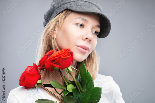 young woman in a cap, blonde with red roses in her hands smiling