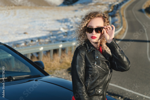 young sexy woman with red lipstick in sunglasses and leather jacket by the car