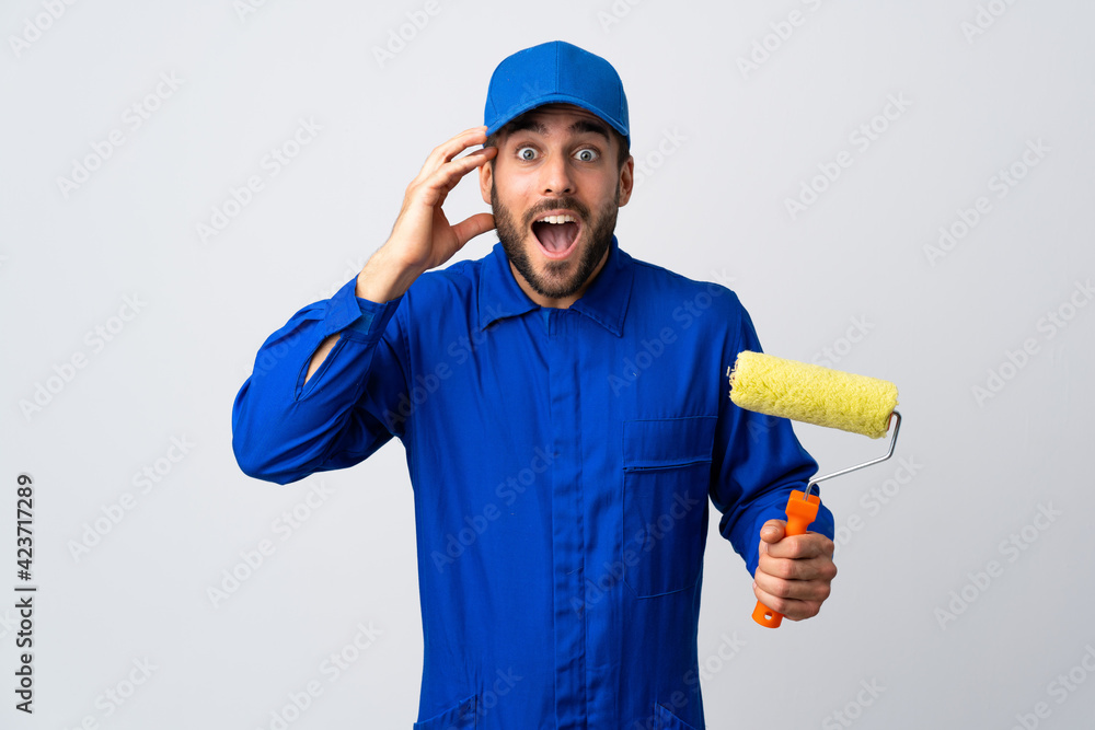 Painter man holding a paint roller isolated on white background with surprise expression