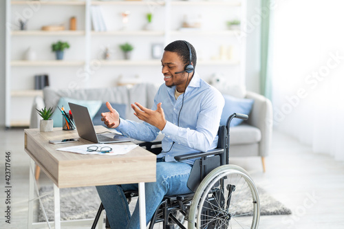 Foto Disabled black guy with headset communicating online on laptop, having business