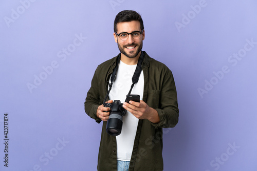 Photographer man over isolated purple background sending a message with the mobile