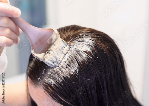 Young woman is coloring her hair in bathroom at home. Close up.  Dyeing hair using a brush. Colouring of grey hair at home. Quarantine and pandemic concept.
