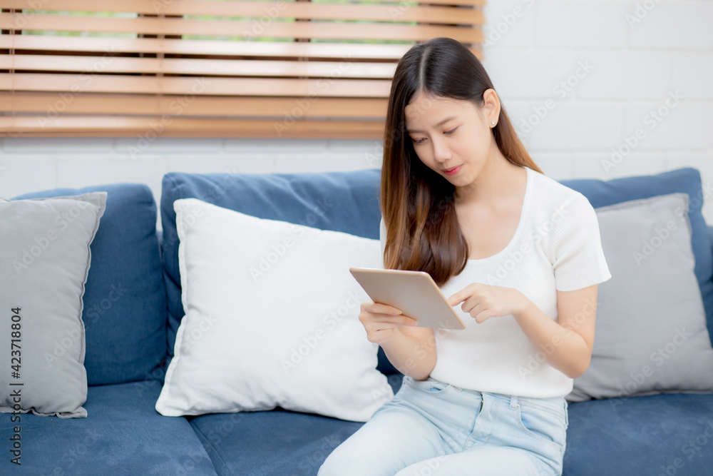 Young attractive asian woman resting using browsing tablet computer on sofa at home, happy girl sitting on couch relax reading digital gadget at house, communication and lifestyle concept. Young attractive asian woman resting using browsing tablet computer on sofa at home, happy girl sitting on couch relax reading digital gadget at house, communication and lifestyle concept.