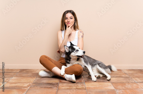 Young pretty woman with her husky dog sitting in the floor at indoors thinking