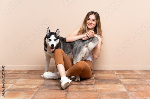 Young pretty woman with her husky dog sitting in the floor at indoors laughing