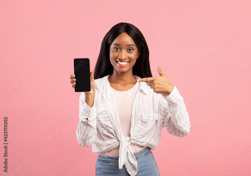 Black woman pointing at cellphone with blank screen on pink background, mockup for mobile app or website design Black woman pointing at cellphone with blank screen on pink background, mockup for mobile app or website design