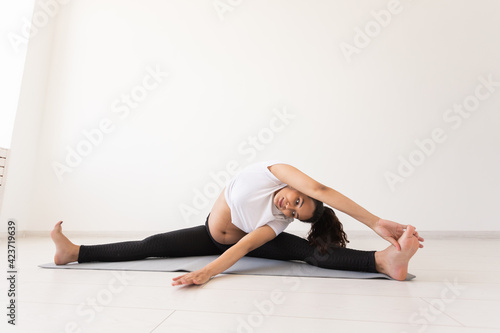 Fototapeta Naklejka Na Ścianę i Meble -  Young flexible pregnant woman doing gymnastics on rug on the floor on white background. The concept of preparing the body for easy childbirth
