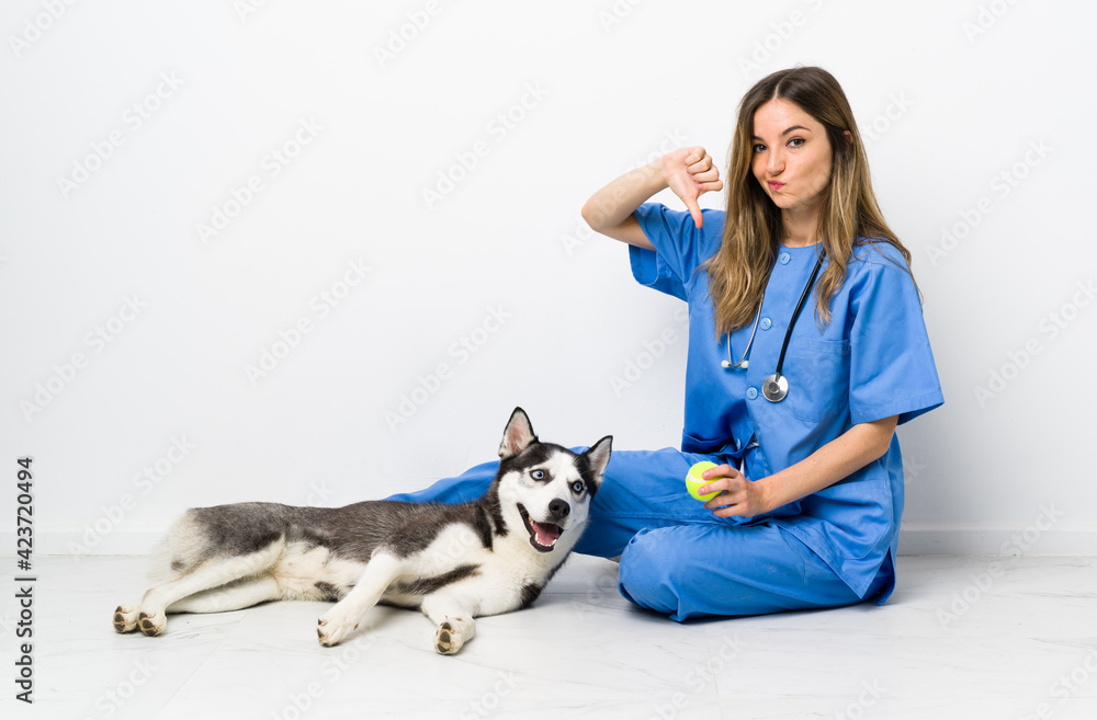 Veterinary doctor with Siberian Husky dog sitting on the floor showing thumb down sign