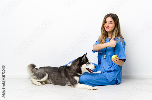 Veterinary doctor with Siberian Husky dog sitting on the floor giving a thumbs up gesture