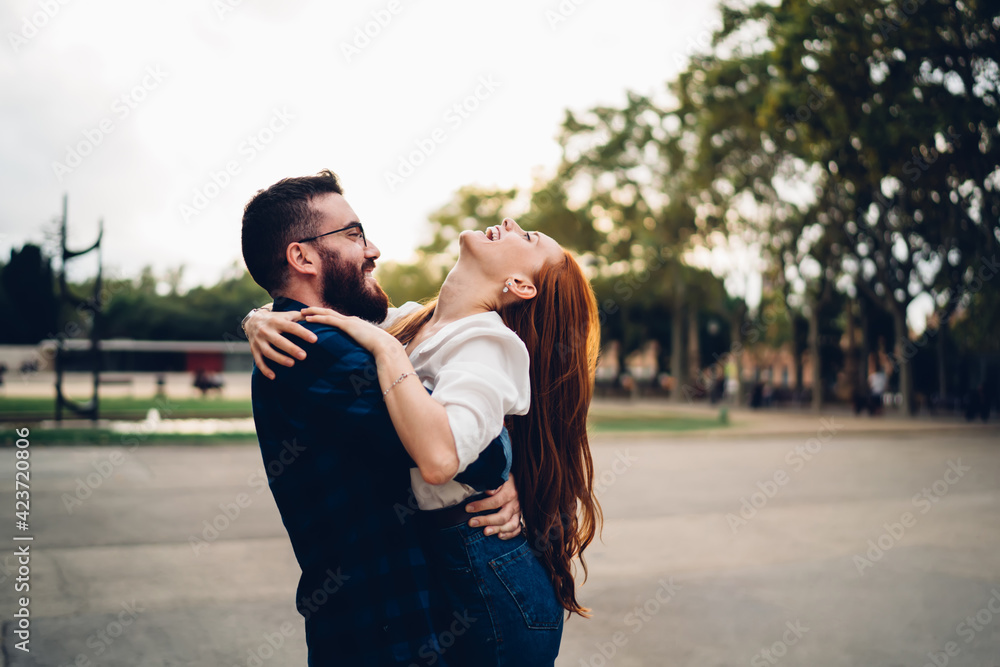 Vivacious female rejoicing and laughing while having fun with cheerful boyfriend holding her in arms, excited Caucasian woman feeling happiness and delight during travel daytime with young husband