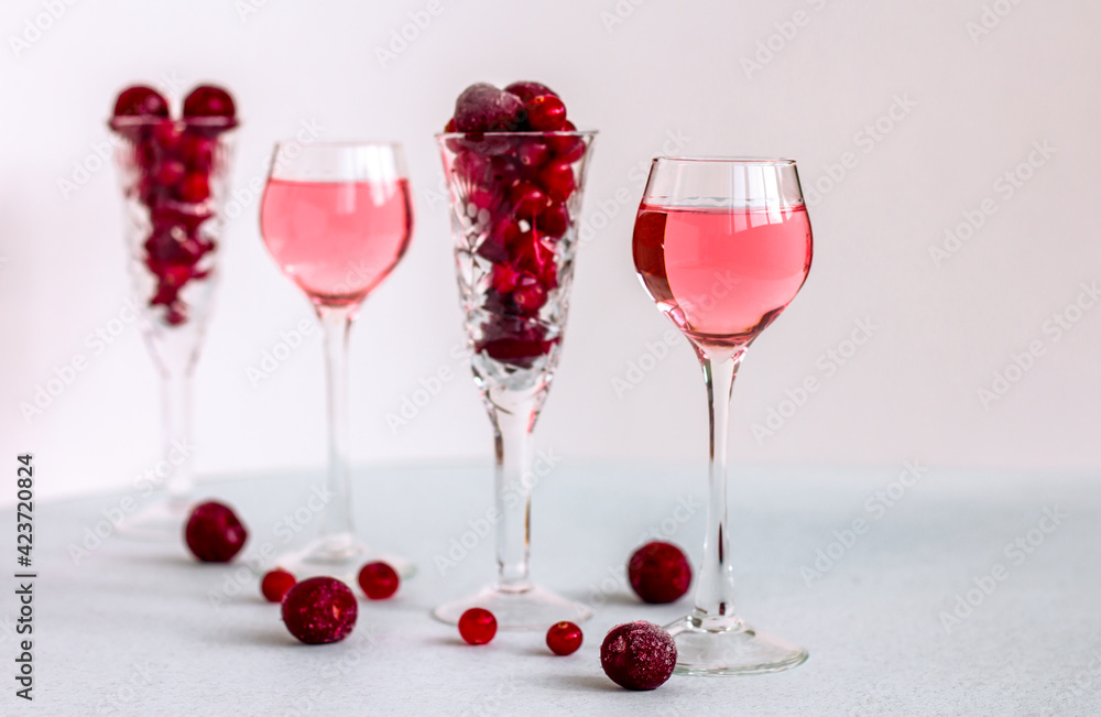 a glasses of pink gin infused with cranberry among crystal glasses of berries on light background, a row of cherry liquor or any red alcoholic cocktail, minimalism a glasses of pink gin infused with cranberry among crystal glasses of berries on light background, a row of cherry liquor or any red alcoholic cocktail, minimalism