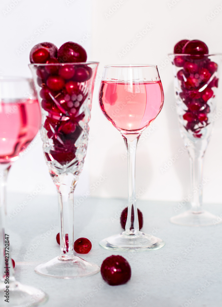 a glass of pink gin infused with cranberry among crystal glasses of berries on white background, cherry liquor or any red alcoholic cocktail closeup a glass of pink gin infused with cranberry among crystal glasses of berries on white background, cherry liquor or any red alcoholic cocktail closeup