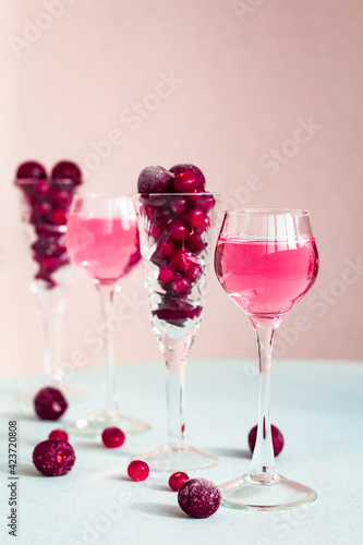 a glasses of pink gin infused with cranberry among crystal glasses of berries on light background, a row of cherry liquor or any red alcoholic cocktail, minimal still life