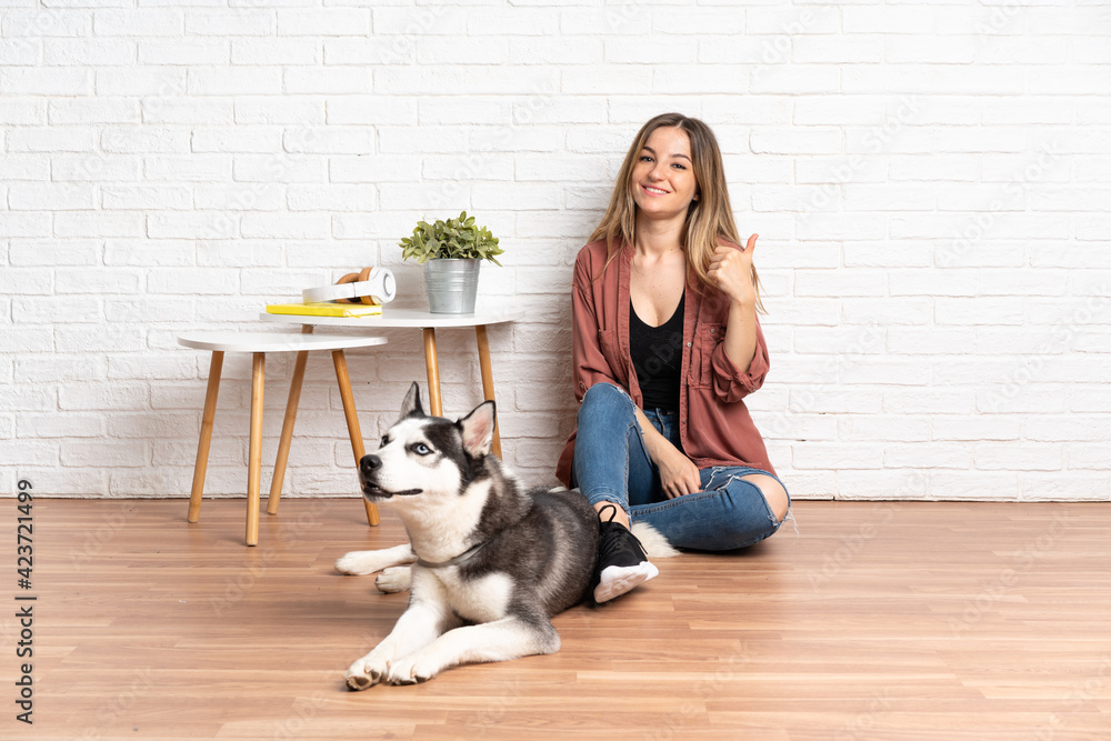 Young girl with her dog sitting in the floor at indoors with thumbs up because something good has happened Young girl with her dog sitting in the floor at indoors with thumbs up because something good has happened