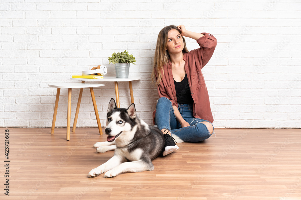 Young girl with her dog sitting in the floor at indoors having doubts and with confuse face expression Young girl with her dog sitting in the floor at indoors having doubts and with confuse face expression