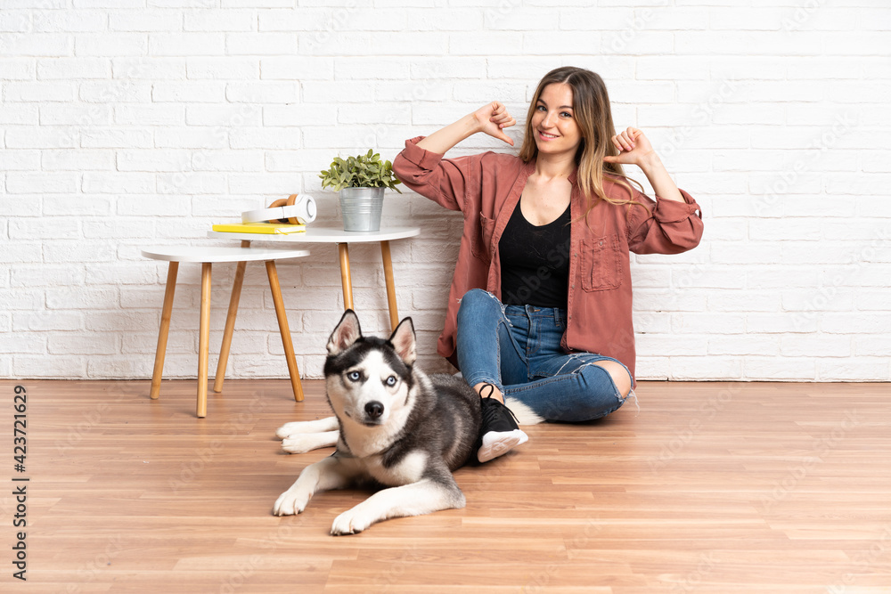 Young girl with her dog sitting in the floor at indoors proud and self-satisfied