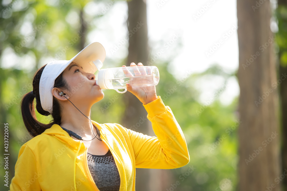 Healthy athletic asian woman is drinking pure water from the bottle refreshing herself after exercise in the nature park Healthy athletic asian woman is drinking pure water from the bottle refreshing herself after exercise in the nature park