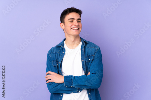 Teenager caucasian handsome man isolated on purple background happy and smiling