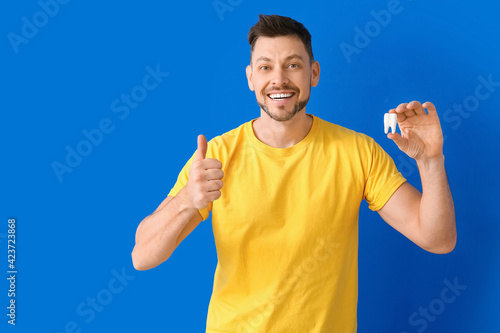 Man with plastic tooth showing thumb-up on color background