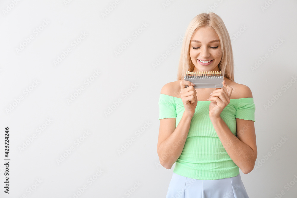 Young woman with teeth color chart on light background Young woman with teeth color chart on light background