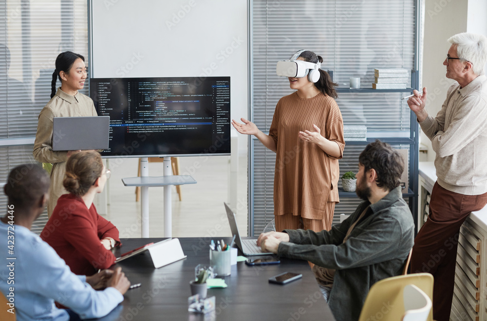 © Seventyfour - Portrait of diverse IT development team working on virtual reality software, focus on smiling woman wearing VR headset in office