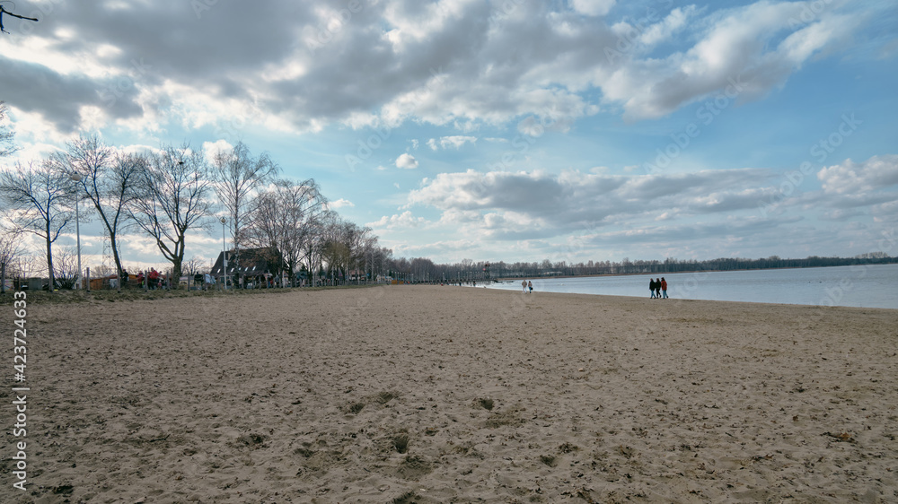 Ludzie spacerujący brzegiem jeziora w czasie wiosennego popołudnia. Na niebie pięknie chmury