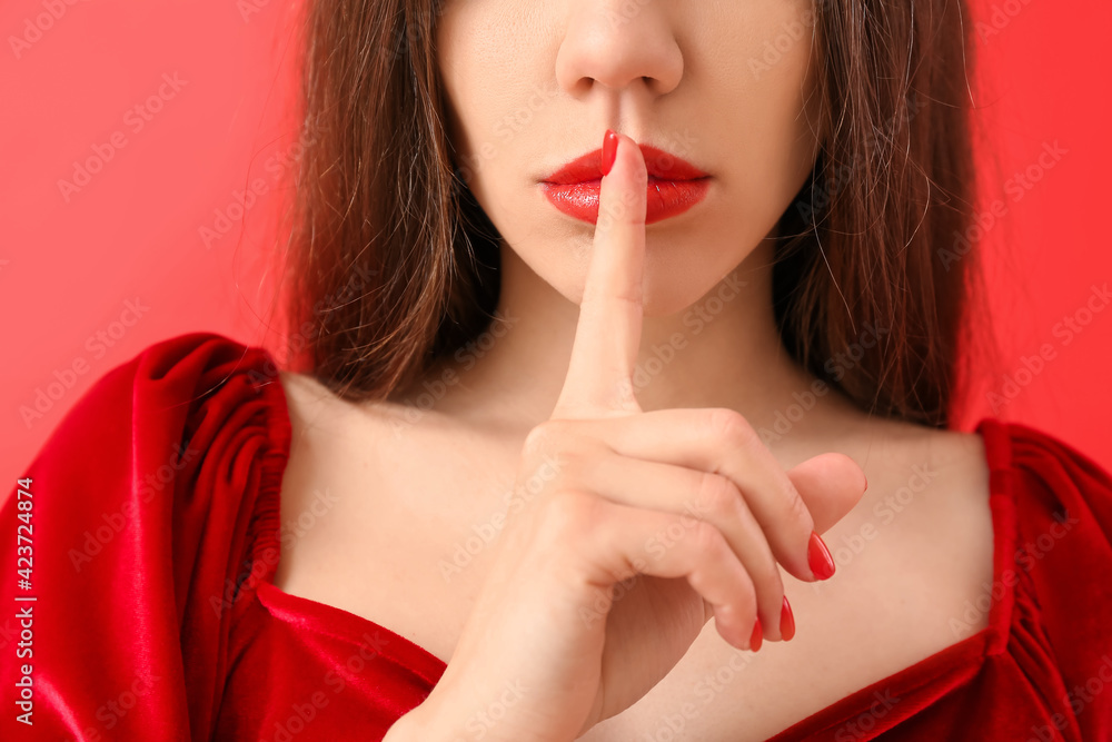 Naklejka premium Young woman with finger on lips, silence and secrecy concept, privacy and quiet gesture, red lipstick and velvet dress