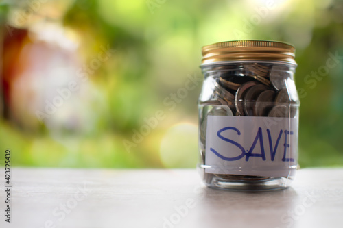 Coins and text SAVE in a glass jar placed on a wooden table. Concept of saving money for investment and emergency situations Or during the coronavirus (COVID-19) outbreak. Close up, Blurred background