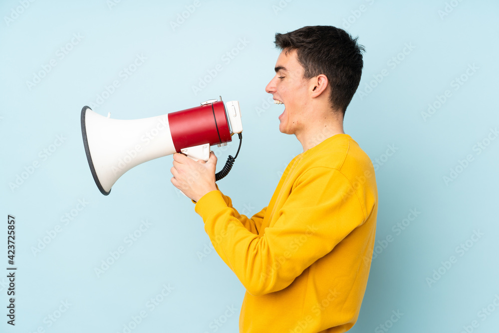 Teenager caucasian handsome man isolated on purple background shouting through a megaphone Teenager caucasian handsome man isolated on purple background shouting through a megaphone