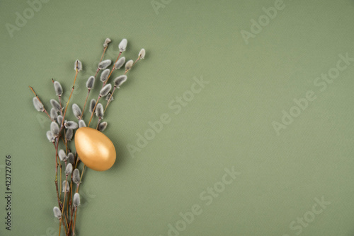 willow twigs and a golden egg on a green background. space for text. top view. easter still life