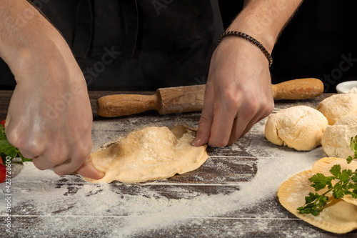 The cook prepares pasties. Step-by-step instruction. Forms the dough. Wooden background.