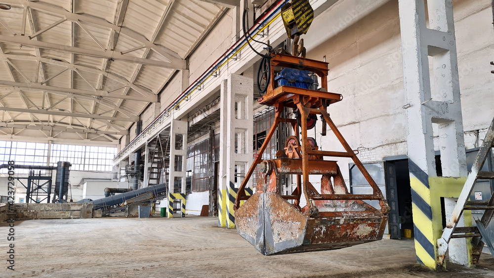 Fototapeta premium Rusty grab bucket or clamshell hanging on crane in empty industrial plant.