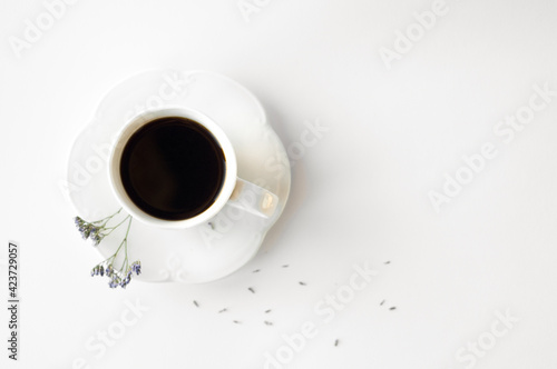 A cup of hot fresh black coffee with foam on a white background. Coffee cup on a round saucer centered inside the frame. Top view with place for text. Morning, energy and vigor concept.