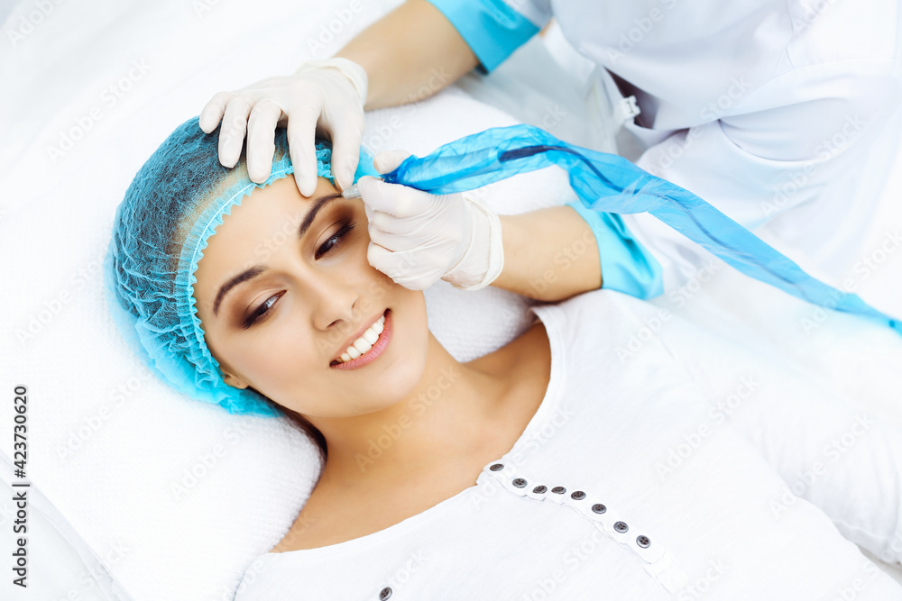 © rogerphoto - Professional beautician doing eyebrow tattoo at woman face. Permanent brow makeup in beauty salon, closeup. Cosmetology treatment
