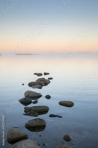 Beautiful sea bay scenery with the row of stones on the calm sunrise colored water and the fog partly hiding view to the sea islands in horizon