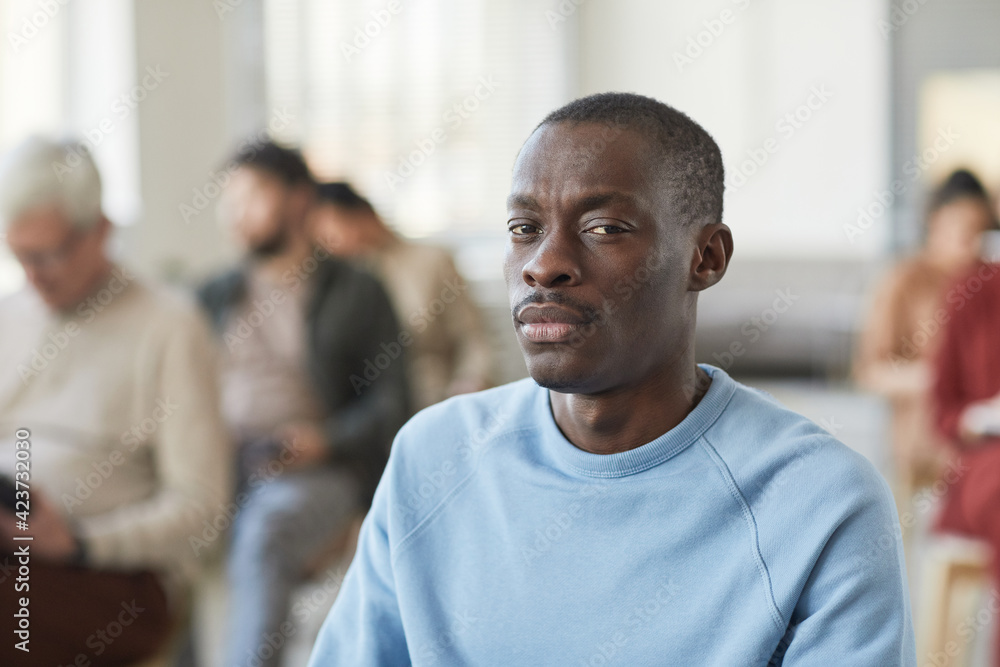 Portrait of serious African-American man looking at camera while sitting in audience with diverse group of people in background, copy space Portrait of serious African-American man looking at camera while sitting in audience with diverse group of people in background, copy space