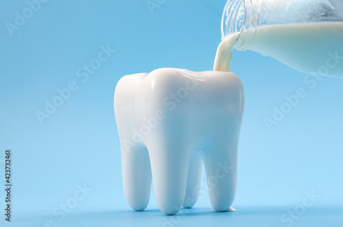 Oral health, cavity prevention and calcium rich drink for strong teeth concept with glass bottle pouring milk into a heathy tooth isolated on blue background