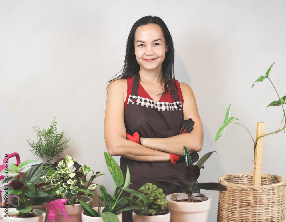 Asian female gardener in sleeveless shirt and apron, working at home, standing with her houseplants indoor, arms crossed,, smiling and looking at camera. gardening concept. Asian female gardener in sleeveless shirt and apron, working at home, standing with her houseplants indoor, arms crossed,, smiling and looking at camera. gardening concept.