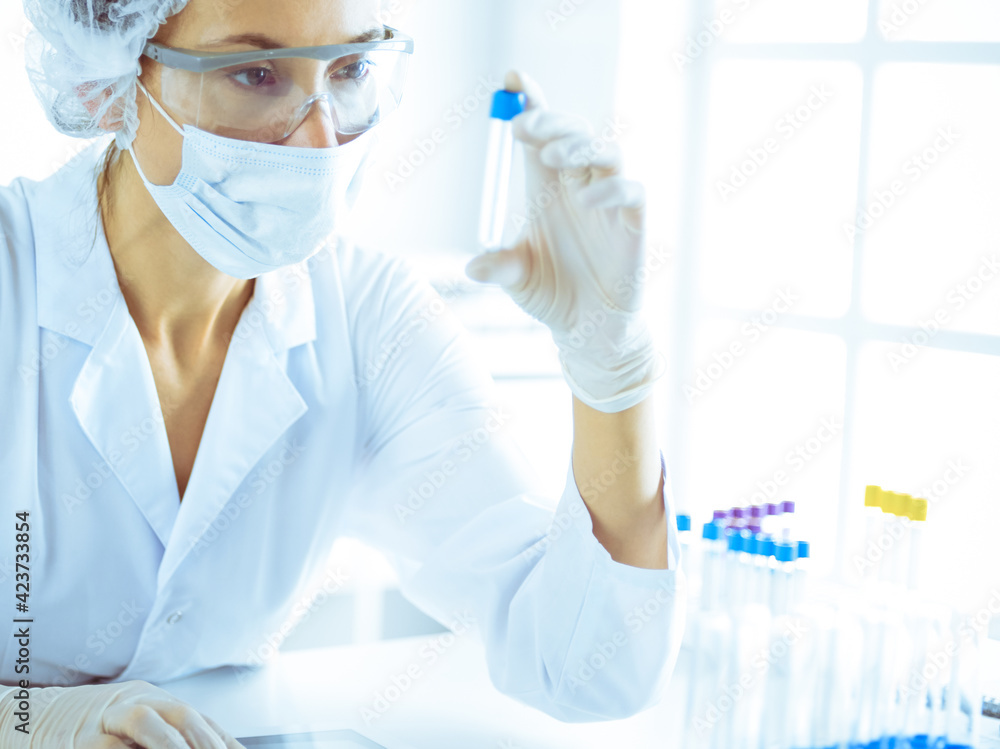 Professional female scientist in protective eyeglasses researching tube with reagents in laboratory toned in blue. Concepts of medicine and science researching Professional female scientist in protective eyeglasses researching tube with reagents in laboratory toned in blue. Concepts of medicine and science researching
