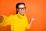 Photo of brown hair optimistic nice girl do selfie hold empty space wear spectacles yellow sweater isolated on orange background